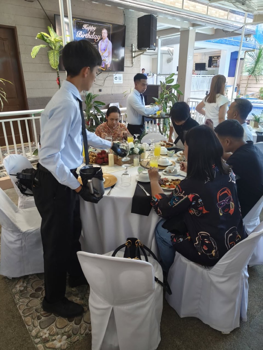 A DLT Catering Services waiter serving a table of seated guests