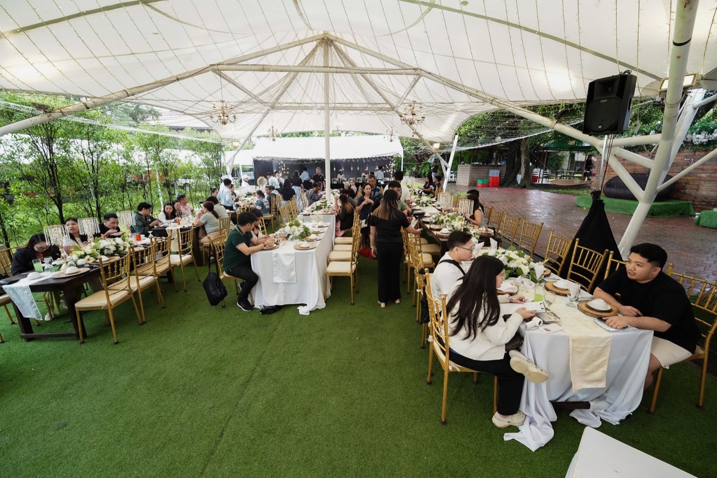 A wide shot of an outdoor white-tent reception full of seated guests