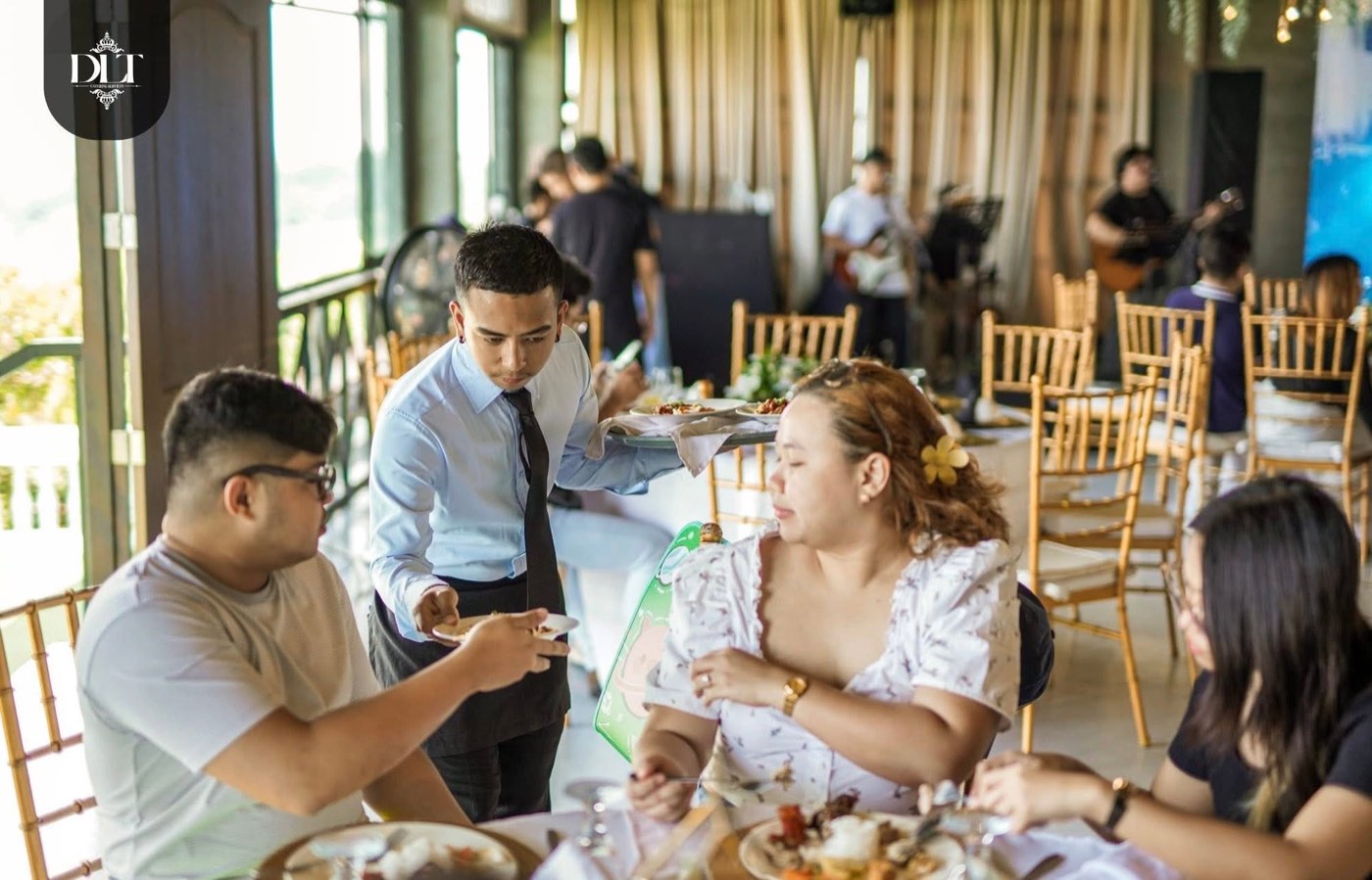 A DLT Catering Services waiter serving plated food to seated guests