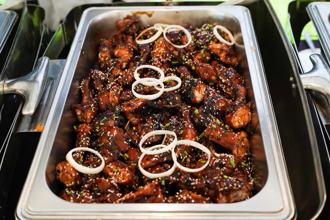 Sesame glazed BBQ chicken with onion rings in a catering tray