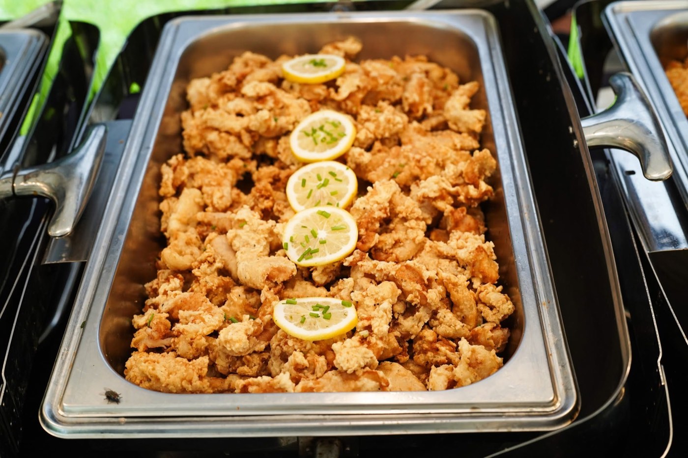 Crispy fried chicken with lemon garnish in a catering tray